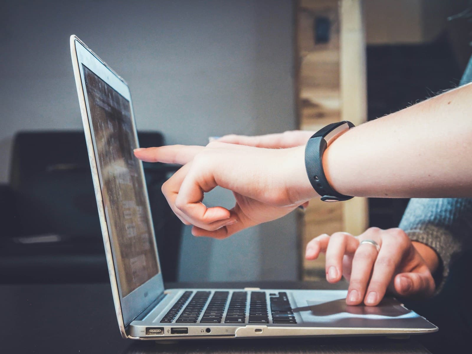 Two hands using a laptop, one finger touching the screen