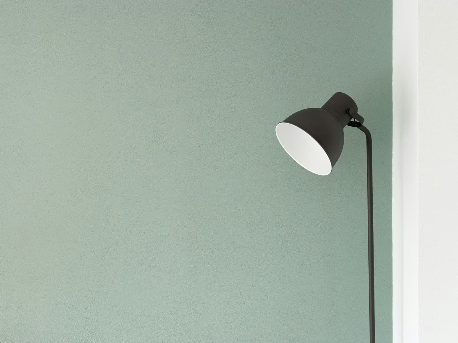 A single black lamp against a pale green wall